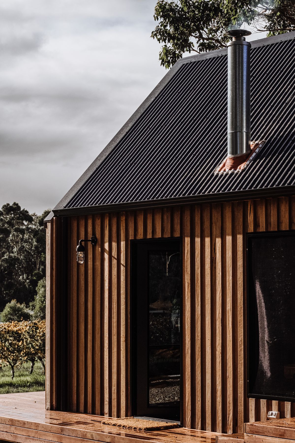 Small vertical timber-clad garden building with black door